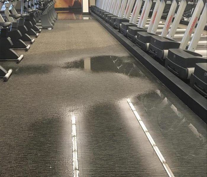 standing water on the commercial flooring with lined equipment on both sides in this fitness center